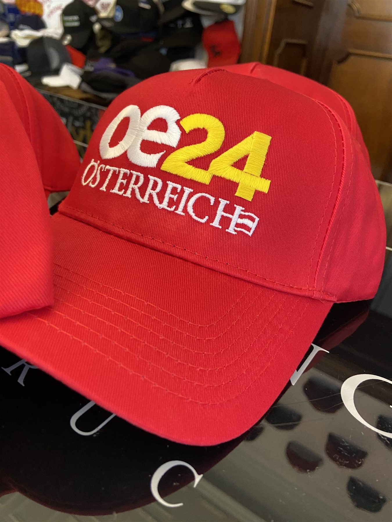Close-up of a red promotional baseball cap with a white and yellow oe24 Österreich logo embroidered across the front panel.